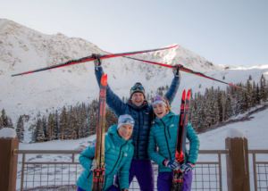 Cross Country team - 3 people holding cross country skis with mountain in background
