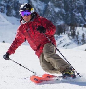 Man in red coat telemark skiing down snowy hill