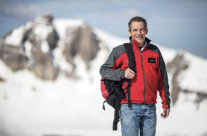 Man with red jack and backpack standing on snowy mountain