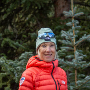woman in red puffy jacket smiling at camera with alpine background