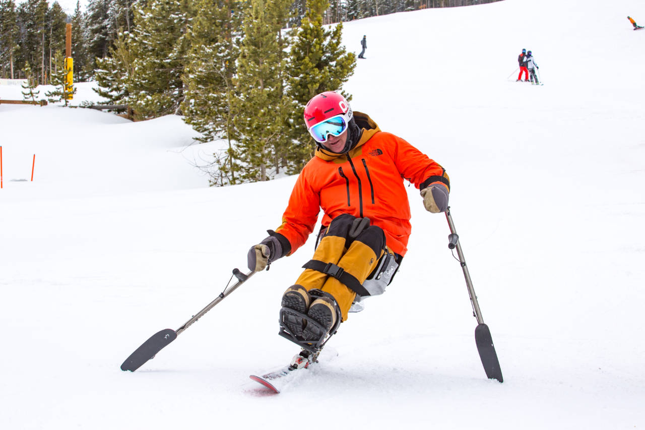 man in sit ski skiing down a snowy hill