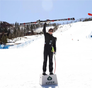 woman in ski gear standing on a podium raising ski in the air