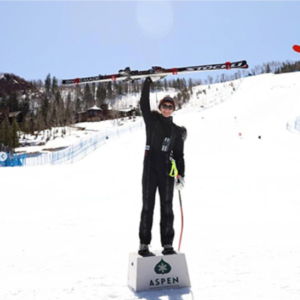 woman in ski gear standing on a podium raising ski in the air
