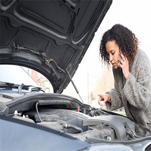 woman on the phone looking under the hood of a car